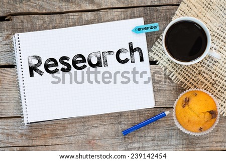 Notebook with research sign and sticker remember on wooden desk with cup of coffee and muffin