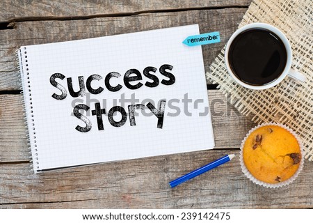 Notebook with success story sign and sticker remember on wooden desk with cup of coffee and muffin