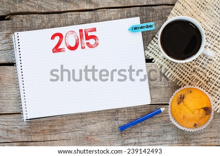 Notebook with 2015 sign and sticker remember on wooden desk with cup of coffee and muffin