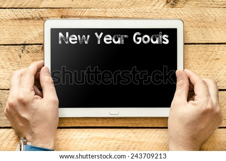 New Year goals on Tablet PC. Hands with Tablet PC with text New Year goals on wooden background