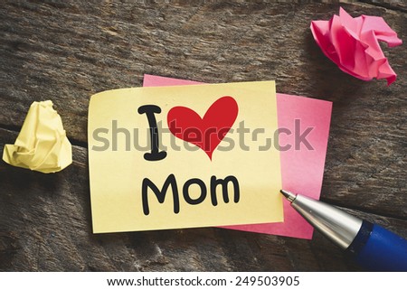 Note with I love Mom. Note with I love Mom and red heart on the wooden background with pen