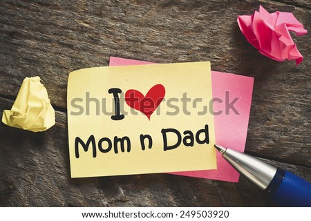 I love mom and dad Note. Note with I love mom and dad with red heart on the wooden background with pen