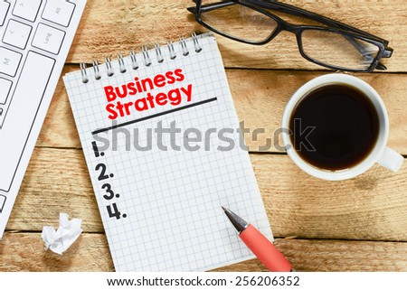 Notebook with business strategy list. Workplace with keyboard , coffee , notebook with business strategy list and pen on wood table