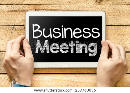 Tablet pc with business meeting. Male hands holding tablet pc with business meeting on wooden background