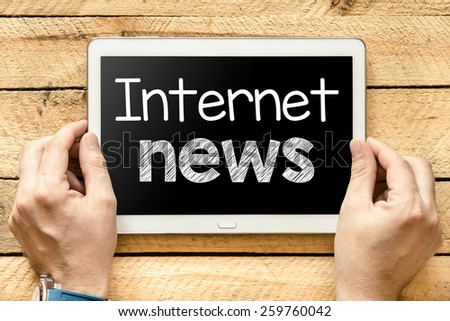 Tablet pc with internet news. Male hands holding tablet pc with internet news on wooden background