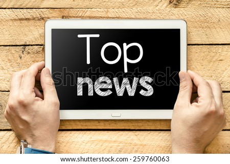 Tablet pc with top news. Male hands holding tablet pc with top news on wooden background