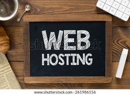 Web hosting handwritten on blackboard. Web hosting handwritten with white chalk on a blackboard, cup of coffee ,croissant, newspaper and calculator on wooden background