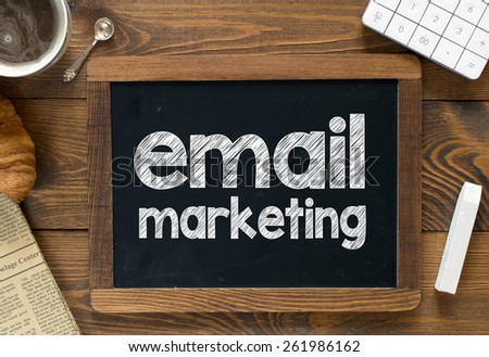 Email marketing handwritten on blackboard. Email marketing handwritten with white chalk on a blackboard, cup of coffee ,croissant, newspaper and calculator on wooden background
