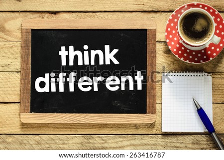 Think different on blackboard. Think different On blackboard with cup of coffee, notebook and pen on wooden background
