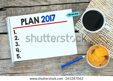 Otebook with plan 2017. Notebook with plan 2017 and sticker remember on wooden desk with cup of coffee and muffin