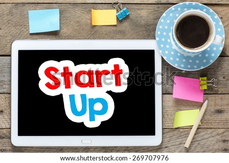 Start up on Tablet computer. Tablet computer with stickers,cup of coffee and start up on the wooden table