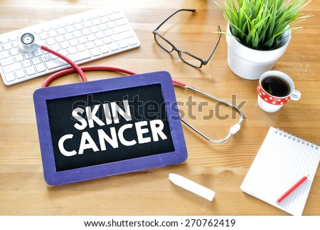 Handwritten skin cancer on blackboard. Handwritten skin cancer with chalk on blackboard,stethoscope, keyboard,notebook,glasses,cup of coffee and green plant on wooden background
