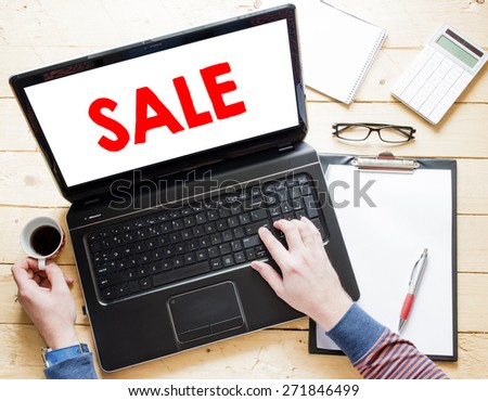 Man hands with laptop and sale sign ,cup of coffee,clipboard,calculator and notepad on wooden table