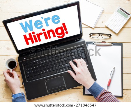 Man hands with laptop and we\'re hiring!,cup of coffee,clipboard,calculator and notepad on wooden table