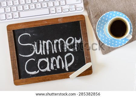 Blackboard with summer camp ,keyboard and cup of coffee on table