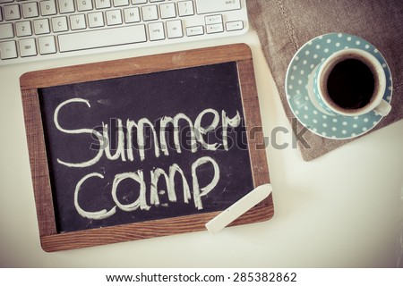 Blackboard with summer camp ,keyboard and cup of coffee on table