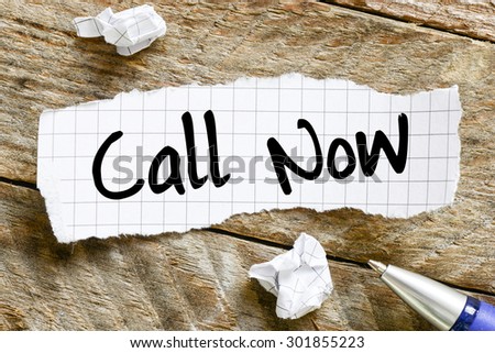 Note with call now on the wooden background with pen