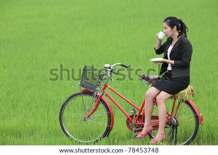 business girl drinking coffee on bicycle,with paddy field background,shallow DOF