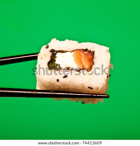 Salmon and cream cheese sushi roll being held in chopsticks. Photographed against a white  studio background.