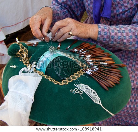 Closeup of pillow with bobbins, pins and hands making bobbin lace