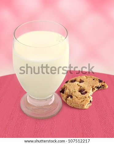 Chocolate Chip Cookie with bite taken and a glass of Milk with pink background.