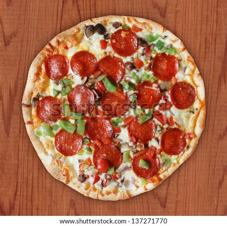 Cooked frozen deluxe pizza with pepperoni, red onion, red pepper, green pepper, mushroom and shredded mozzarella cheese on wood background.