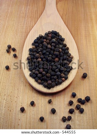 Black Peppercorns on a wooden spoon.