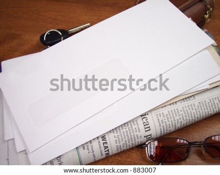 Stack of Mail (blank envelope on top) with newspaper, on table with everyday objects.