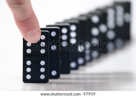 Finger ready to push over dominoes. Only the first domino in focus.