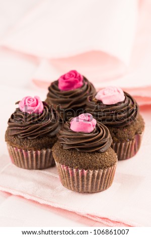 Group of delicious chocolate cupcakes decorated with red and pink roses over a pink tablecloth