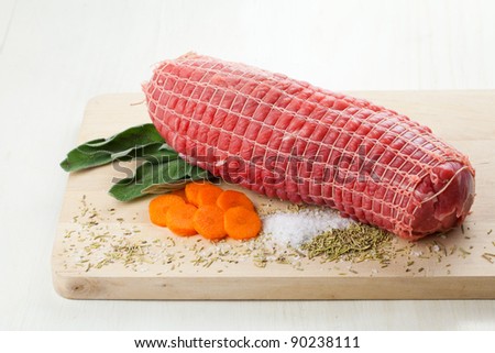 Raw meet roll with sage, carrots, rosemary and salt, over a wood board and ready to be roasted