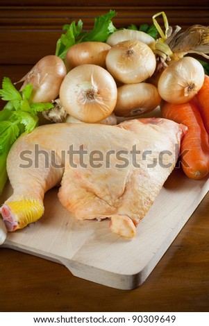 Raw chicken leg, onions, carrots and celery over a chopping board and an antique kitchen cabinet