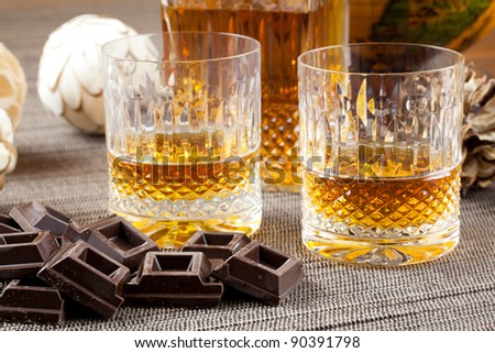 Dark chocolate and fine bourbon whiskey in crystal bottle and tumbler glasses with stylish spheres and antique globe in background