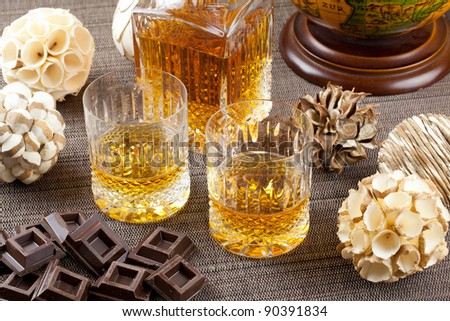 Dark chocolate and fine scotch whisky in crystal bottle and tumbler glasses with stylish spheres and antique globe in background