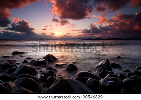 Long exposure shot of beautiful sunrise in Maui, Hawaii. Black lava stones in foreground against a quiet ocean and sun in background