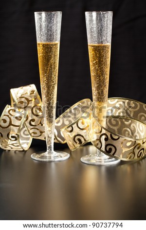 Two stylish glass of champagne with gold festive decorations against black background