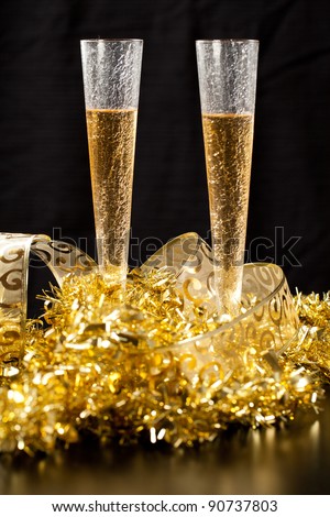 Two stylish glass of champagne with gold festive decorations against black background