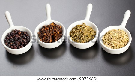 Assorted dry herbs and spices in white bowls over a black board