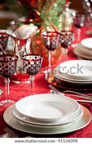 Elegant place setting with white dishes over a red table cloth plus goblet and decorations