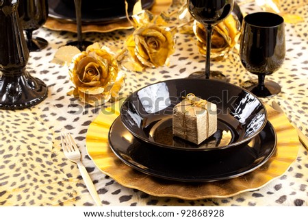 Golden gift box in a black and gold table setting with gold roses over a leopard tablecloth