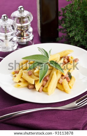 Delicious plate of penne pasta with ham and potatoes. Served in a modern dishware over a violet table setting