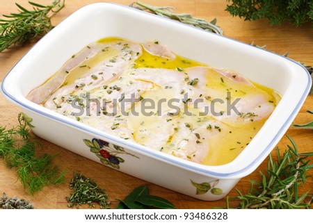 A casserole with sliced chicken breast, marinating with herbs, salt, pepper, olive oil and lemon
