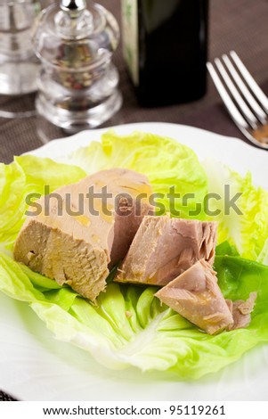 Chunk of tuna fish in a lettuce bed, served in an elegant place setting