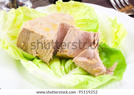 Chunk of tuna fish in a lettuce bed, served in an elegant place setting