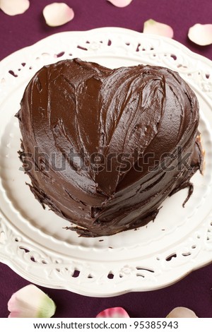 heart shaped chocolate cake in a traditional dish over a purple table cloth decorated with rose petals