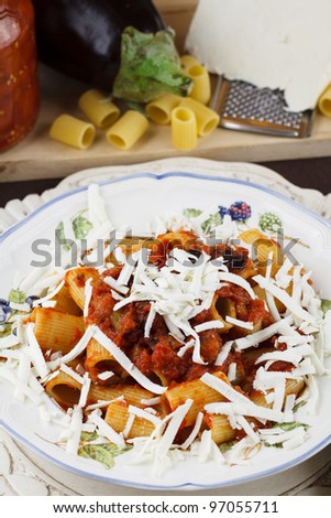 Traditional recipe from Sicily, Italy, pasta Norma. Macaroni with tomato and eggplant sauce topped with freshly grated ricotta cheese. Raw ingredients in background