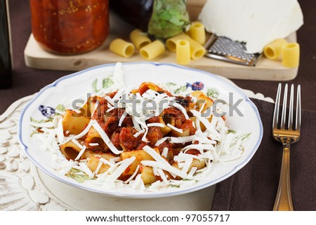 Traditional recipe from Sicily, Italy, pasta Norma. Macaroni with tomato and eggplant sauce topped with freshly grated ricotta cheese. Raw ingredients in background