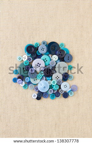 Many blue sewing or clothing buttons piled up on hessian