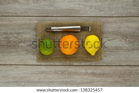 A group of three different citrus fruits lined up next to each other (lime, orange, lemon) with zester tool on burlap and weathered boards