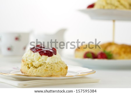 English Cream tea scene with scone offset, Devonshire style, on china plate with cake stand behind. Part of a series showing the preparation of scones.